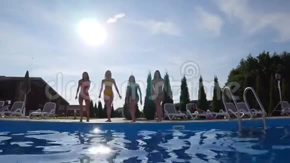 快乐潜水一群女朋友在夏季露台上慢动作地在蓝色游泳池里奔跑和跳跃视频的预览图