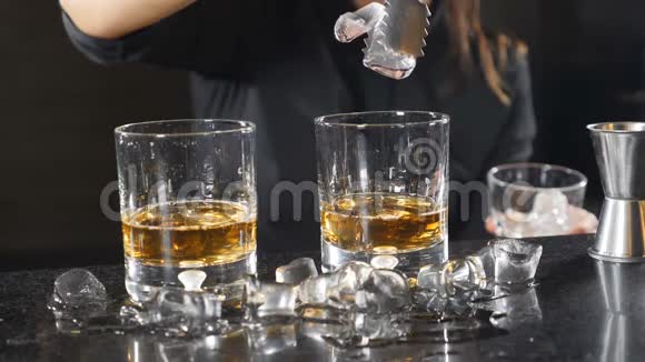 女酒保慢慢地把冰块和威士忌放进杯子里冰飞溅而下年轻女子视频的预览图