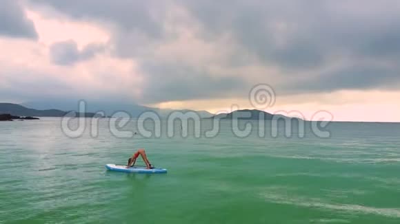 女孩站在海洋中的桨板上向前弯曲视频的预览图