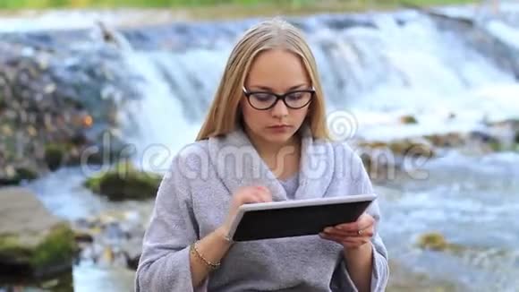 女孩用笔记本电脑工作在瀑布附近吃苹果视频的预览图