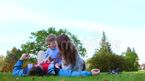 幸福的家庭躺在草坪上爸爸妈妈和儿子一起玩孩子笑了在此背景下视频的预览图