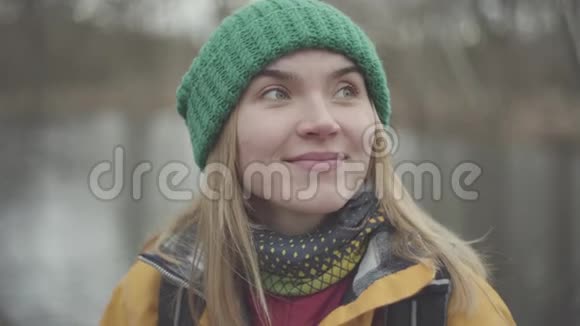 公园里戴着绿帽子穿着黄色外套从热水瓶里喝茶或喝咖啡的可爱女人的画像视频的预览图