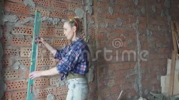 穿着格子衬衫和蓝色牛仔裤的年轻苗条的女人将在墙的背景下测量一个视频的预览图
