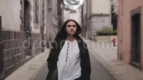 一个年轻漂亮的棕色头发的长发女人走在一条狭窄的镇街上慢动作视频的预览图