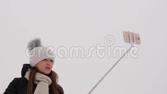 年轻女孩在智能手机和自粘上拍照在冬季公园圣诞节早上快乐的女孩走进来视频的预览图