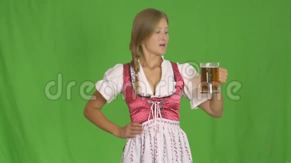 年轻的啤酒节女服务员穿着传统的巴伐利亚礼服在绿色背景下提供大啤酒杯视频的预览图