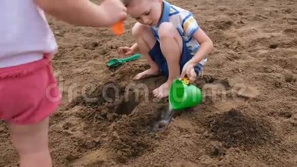 小男孩把水桶里的水倒进沙子的一个洞里孩子们在沙滩上玩耍视频的预览图