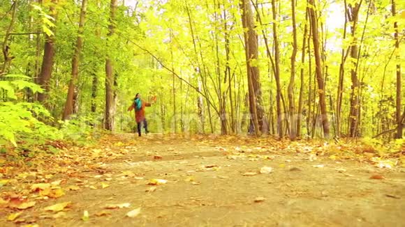 秋天公园里一个穿着外套和围巾手里拿着枫叶的年轻黑发女人沿着小路跑着一头扑了上来视频的预览图