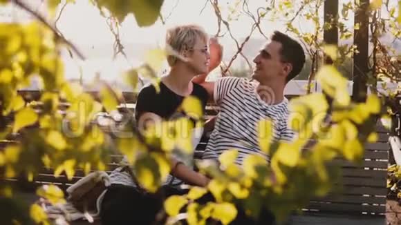在美丽的阳光明媚的秋日慢动作甜蜜浪漫的情侣坐在一起玩在公园的长凳上聊天视频的预览图