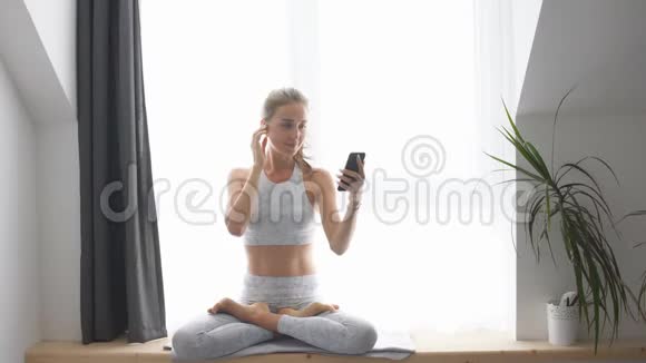 女人坐在窗台上看智能手机和耳机上的视频视频的预览图