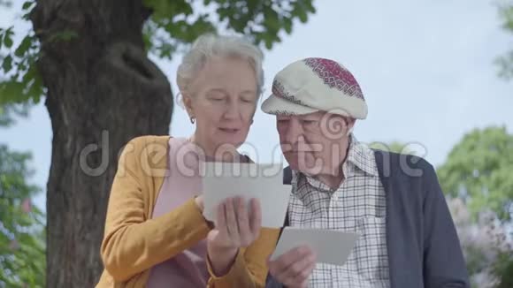 肖像可爱的成熟女人和男人看着老照片回忆着坐在公园长凳上的快乐时刻视频的预览图