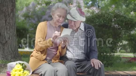 肖像可爱的成年夫妇看着老照片回忆着坐在公园长凳上的快乐时刻成熟成熟视频的预览图