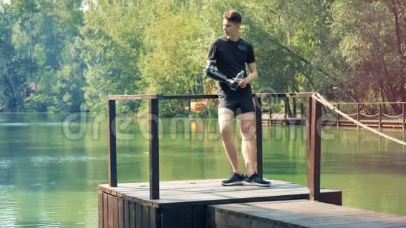 一个人喝水用他的假肢站在池塘附近4K视频的预览图