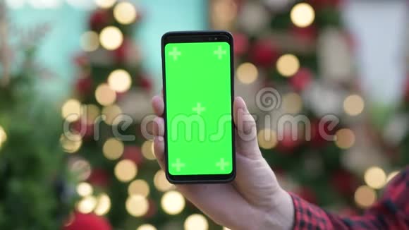 年轻人用带绿色屏幕的手机在户外的圣诞树上视频的预览图