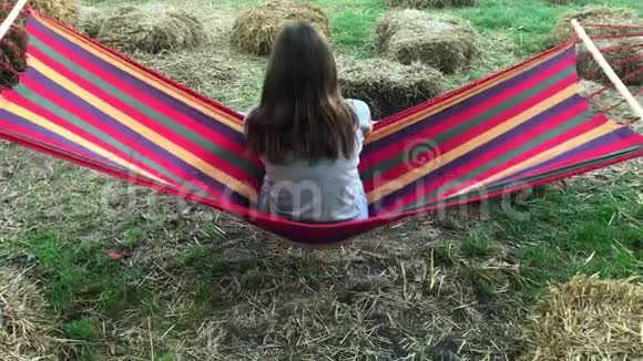 夏天美丽可爱的小女孩在公园或户外的彩色吊床上休息视频的预览图