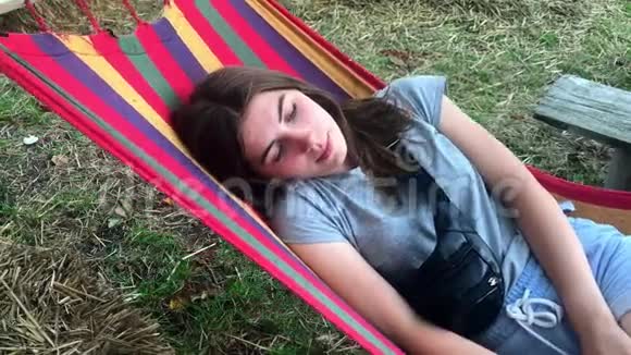 夏天美丽可爱的小女孩在公园或户外的彩色吊床上休息视频的预览图