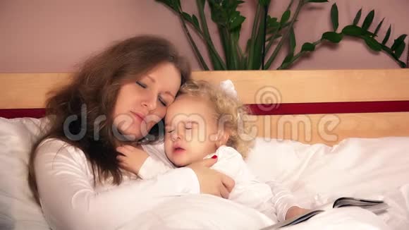 可爱的卷发小女孩睡在白床上和妈妈拥抱视频的预览图