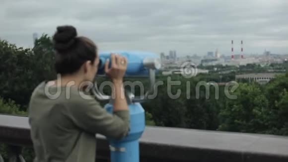 一个美丽的女孩通过旅游望远镜观看城市景观的侧面景色视频的预览图