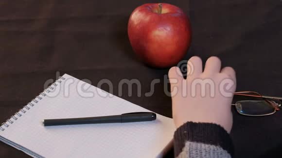 手少年特写那个年轻人从桌子上举起眼镜一个红苹果一个笼子里的记事本和一支钢笔躺在上面视频的预览图