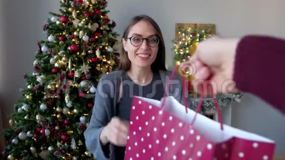 戴眼镜的幸福女人在装饰好的家中在圣诞树的背景上收到圣诞礼物新年快乐视频的预览图