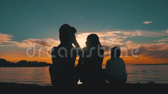 年轻父母的剪影带着两个孩子在海滩上看日落人们在海上玩得很开心概念视频的预览图