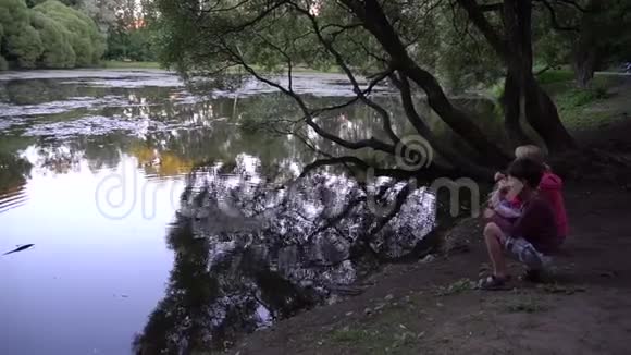 妈妈和儿子坐在池塘边喂鸭子视频的预览图