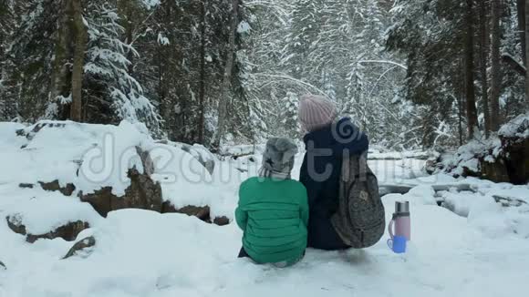 妈妈和儿子坐在一起拥抱在白雪覆盖的森林里冬季阴天后景视频的预览图