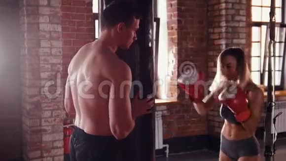 健身房里的男人和女人教练拿着一个拳击袋女人打了它视频的预览图
