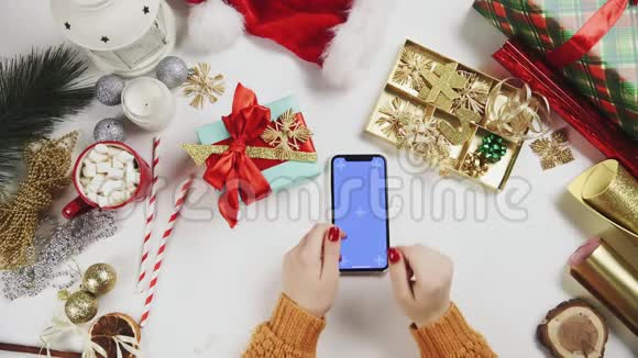 女士使用智能手机与Chroma键点击滑动滚动向上白色桌子上的圣诞装饰视频的预览图