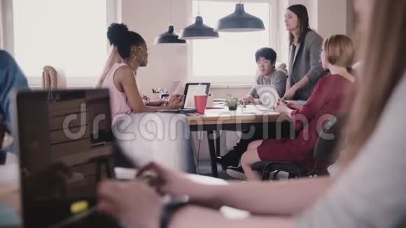 无法辨认的女孩在笔记本电脑上打字以现代多民族阁楼办公室为背景进行头脑风暴视频的预览图