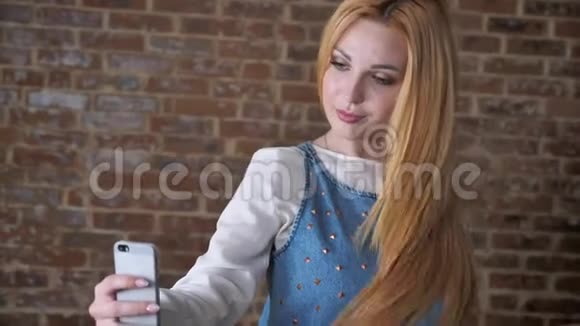 年轻可爱的金发女孩在智能手机上自拍砖背景交流理念视频的预览图