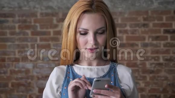 年轻迷人的金发女孩正在智能手机上输入信息在镜头下观看砖背景交流理念视频的预览图