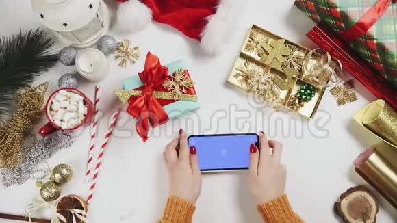 女士使用智能手机与Chroma键点击滑动滚动向上白色桌子上的圣诞装饰视频的预览图
