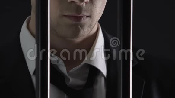 愤怒的商业罪犯站在监狱牢房的金属栏杆后面贿赂视频的预览图
