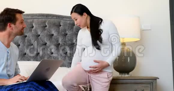 在卧室4k的床上使用笔记本电脑的怀孕夫妇视频的预览图