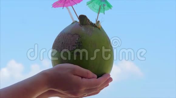 年轻的双手女人在热带海滩上的美丽的云彩背景中抱着椰子暑假的概念视频的预览图
