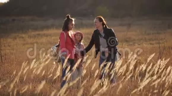 日落时分一位快乐的母亲和她的两个女儿在草原上漫步视频的预览图