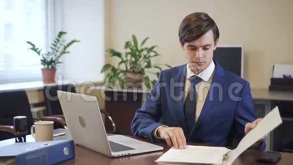 商人在笔记本电脑上工作在现代办公室里拿纸质文件视频的预览图