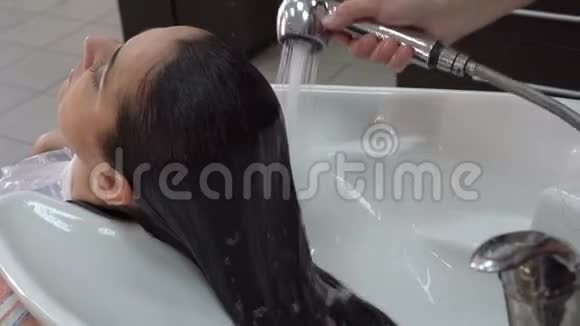 发型师用水槽上的发廊里水把女孩的头倒掉然后洗了视频的预览图
