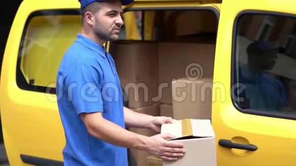 穿蓝色制服的送货员在黄色卡车附近持有纸箱视频的预览图