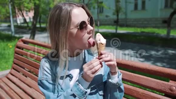 年轻女孩坐在长凳上手上拿着冰淇淋穿着白色T恤牛仔布牛仔裤和太阳镜视频的预览图