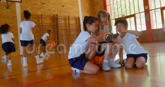 4k学校篮球场上使用数码平板电脑的学童视频的预览图