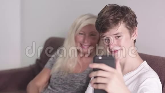 老祖母和成年孙子用手机在沙发上坐下视频通话视频的预览图