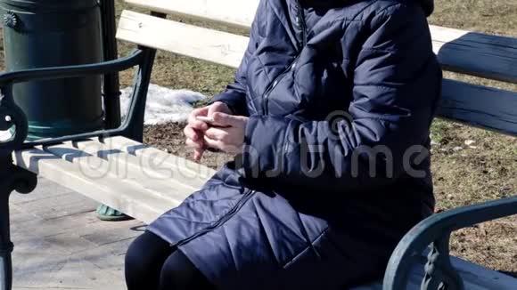 一位年长的妇女坐在公园户外的长凳上使用敲击智能手机她正在用智能手机视频的预览图