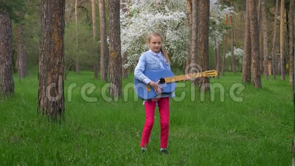 可爱的小女孩站在春天公园弹吉他音乐视频的预览图
