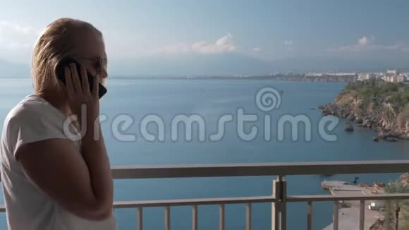 一位白发苍苍的女士在海边的一个酒店阳台上和一个电话交谈视频的预览图