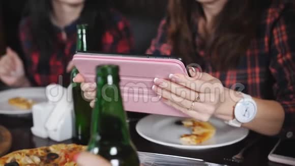 四个女孩在餐厅里在平板上观看照片餐厅里有披萨和啤酒视频的预览图