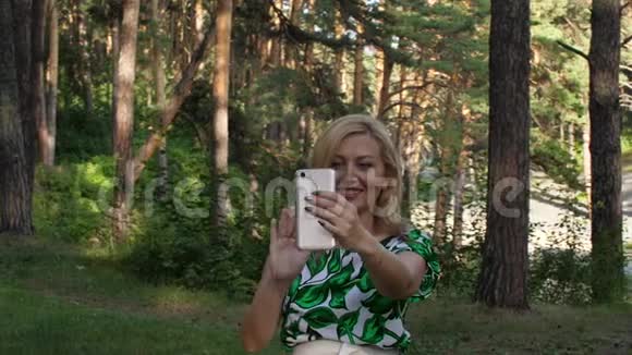 在森林户外与智能手机视频聊天的快乐女人视频的预览图
