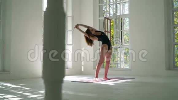 苗条的白种人女人站在白色的大房间里的垫子上练习瑜伽运动健身的年轻女子视频的预览图