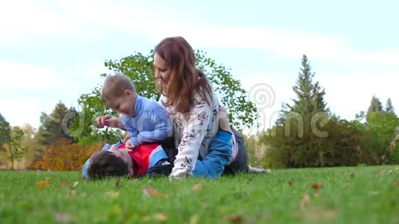 幸福的家庭躺在草坪上爸爸妈妈和儿子一起玩孩子笑了在此背景下视频的预览图